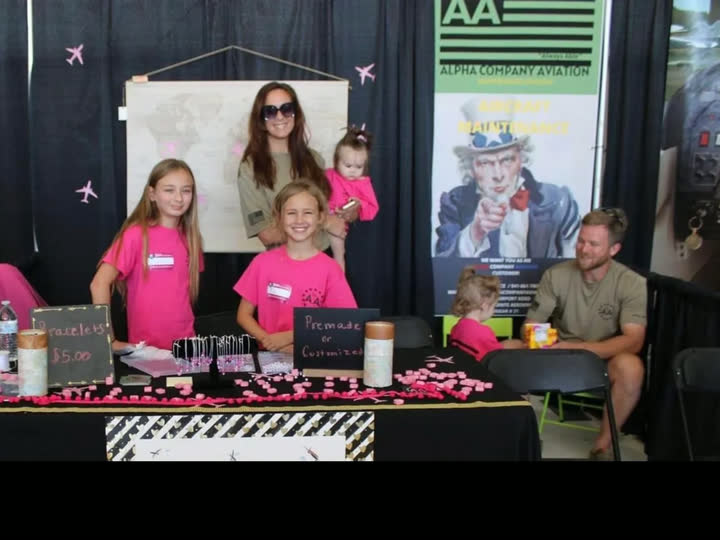 Elena Awad and her husband with their daughters at a Florida community event, Alpha Company Aviation booth in the background